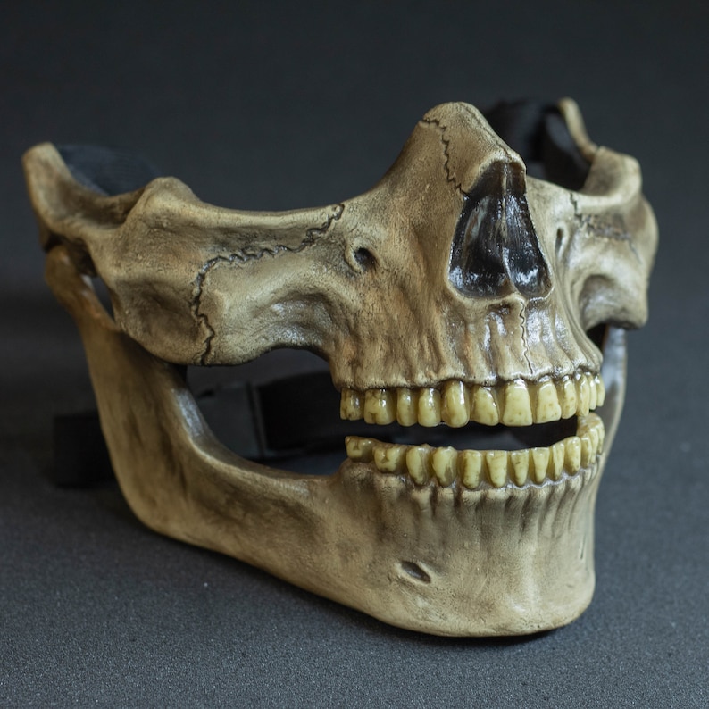 Pu&ograve; includere: Una maschera a teschio dettagliata, a mezza faccia, in un colore simile all'osso invecchiato. La maschera presenta denti realistici, cavit&agrave; nasale e orbite, con suture visibili e un cinturino nero per il fissaggio. Tema Halloween o costume.