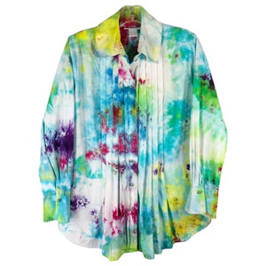 May include: A long-sleeved button-up shirt with a tie-dye pattern in shades of blue, green, pink, and purple. The shirt has a pleated front and a collared neckline.