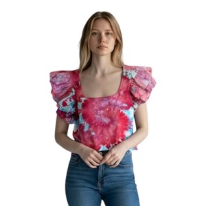 May include: A tie-dye top with a square neckline and ruffled sleeves. The top features a vibrant pattern of red, pink, and blue hues. The model is wearing blue jeans.