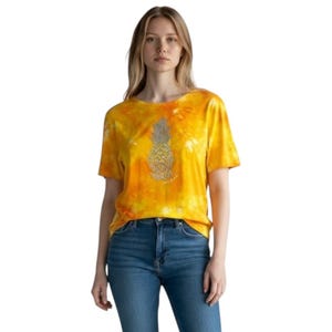 Könnte beinhalten: Gelb-oranges T-Shirt mit Batikmuster und einem detaillierten silbernen Ananas-Motiv. Das Ananas-Design weist komplizierte Details auf. Das T-Shirt wird mit einer blauen Jeans getragen.