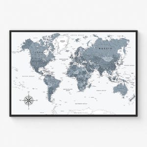May include: A framed world map in grey and white. The map shows continents, countries, and oceans, with a compass rose in the lower left corner. The map is set against a white background and framed in black.