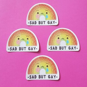 May include: Four rainbow stickers with a sad cartoon face and the text "Sad but Gay" on each.