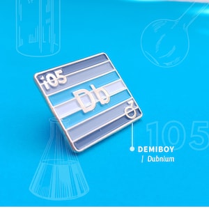 Puede incluir: Un pin de esmalte plateado con un diseño a rayas azul, blanco y gris. El pin presenta el símbolo químico "Db" y el número "105" encima. El texto "DEMIBOY | Dubnium" está impreso debajo del pin.