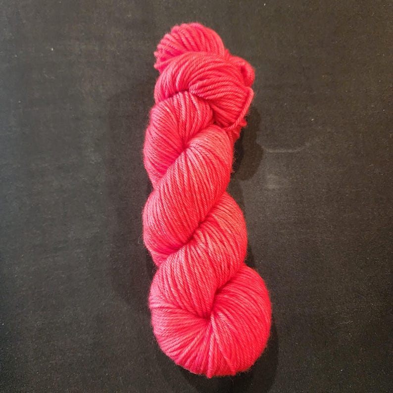 May include: A skein of bright red yarn, tightly wound and twisted, set against a dark backdrop. The yarn looks soft and fluffy, suitable for knitting or crochet. The colour is a vivid, solid red, perfect for various crafting projects.