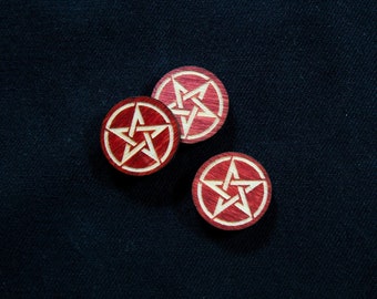 Könnte beinhalten: Drei rote Holz-Pentagramm-Token mit weißen Umrissen auf schwarzem Hintergrund.
