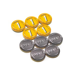 May include: A collection of circular game tokens consisting of five yellow tokens marked with the number 1 and four grey tokens embossed with the word SPENT. The tokens are arranged in a cluster, featuring a smooth, glossy finish on their surfaces.