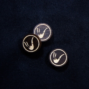 May include: Three wooden round discs with a white pipe design on a dark blue background.