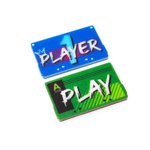 May include: Two rectangular acrylic plaques. The blue plaque features a large light blue number 1 and the text PLAYER with a small crown icon. The green plaque features the text PLAY and the label A SIDE in a black box with diagonal lines.