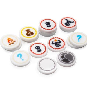May include: A collection of white, circular game tokens with various colorful icons. The tokens feature images of a skull, question mark, money bag, fire, and other symbols. The tokens are designed for board games or tabletop games.
