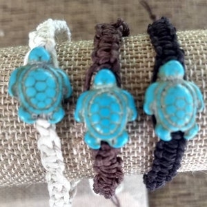 May include: Three bracelets with turquoise turtle charms. The bracelets are made of white, brown, and black cord.