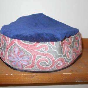 Può includere: Un cappello di velluto blu con un ricamo floreale rosa e grigio.