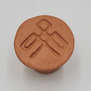 Puede incluir: Un pomo redondo de terracota con un diseño geométrico. El pomo es de color marrón claro.