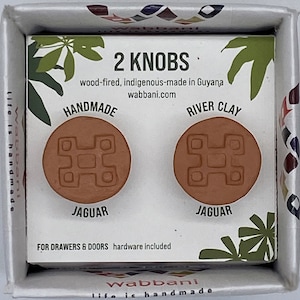 Könnte beinhalten: Zwei handgefertigte Schrankknöpfe aus Ton mit einem Jaguar-Design. Die Knöpfe sind aus Flusslehm und werden mit Holz gebrannt. Der Text auf der Verpackung lautet "2 Knöpfe", "Handgefertigt", "Flusslehm", "Jaguar", "Für Schubladen & Türen", "Hardware inklusive" und "wabbani.com".