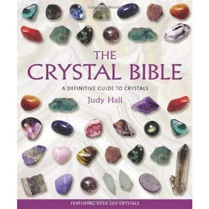 May include: The Crystal Bible book cover featuring a collection of colorful crystals. The title is in large purple letters, with the author's name, Judy Hall, below. The cover also states "A Definitive Guide to Crystals" and "Featuring Over 200 Crystals".