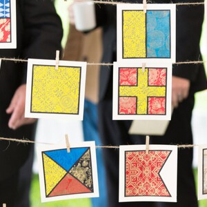 May include: A string of colorful fabric squares with different patterns, hanging from a rope with clothespins. The squares are yellow, blue, red, and white, and have a variety of geometric and floral designs.