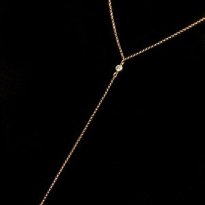 May include: A delicate gold-toned necklace with a Y-shaped design. The necklace features three small, clear gemstones. The chain is fine and hangs against a black background, creating a simple yet elegant look.
