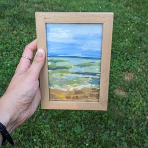 May include: A framed painting depicting a seascape with a blue sky, green water, and a sandy beach.