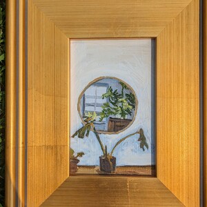 May include: A framed painting of a plant in a pot, with a circular window behind it showing a view of another plant. The painting is in a gold frame with a dark grey inner border.