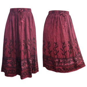 May include: Two burgundy maxi skirts with a drawstring waist and black floral embroidery. The skirts have a flowing, A-line silhouette and are made of a crinkled fabric. The embroidery features a repeating pattern of stylized plants.