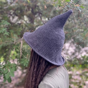 May include: A dark gray crocheted witch hat with a pointed crown. The hat is worn by a person with long dark hair.