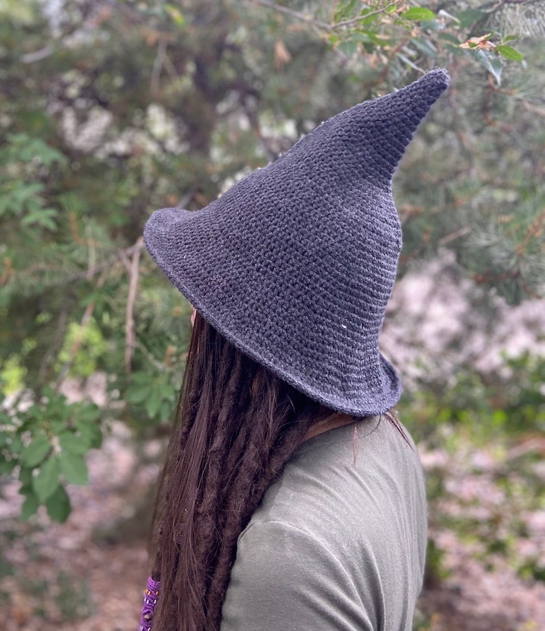 May include: A dark gray crocheted witch hat with a pointed crown. The hat is worn by a person with long dark hair.