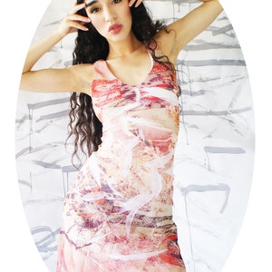 Puede incluir: Una mujer lleva un vestido sin mangas con estampado floral de colores. El vestido tiene un escote en V y una silueta ajustada. El fondo es una pared blanca con salpicaduras de pintura gris.