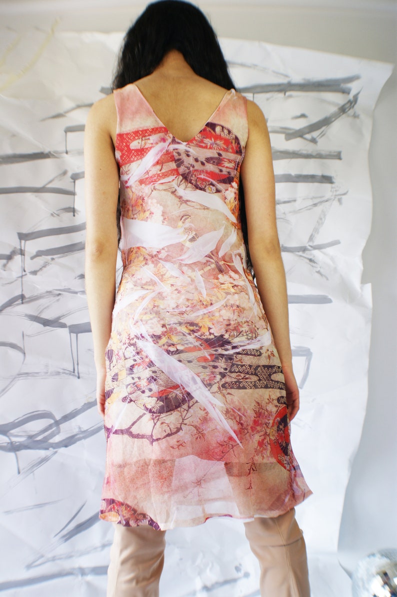 Puede incluir: Un vestido transparente sin mangas con estampado floral y geom&eacute;trico en tonos rosa, rojo, blanco y marr&oacute;n. El vestido tiene un escote en V y una silueta fluida.