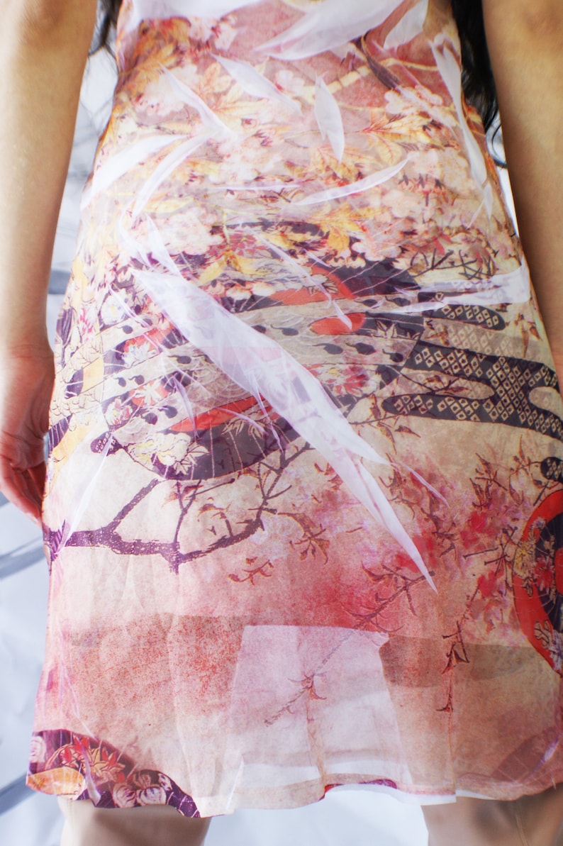 Puede incluir: Un vestido blanco transparente con estampado floral en tonos rosa, rojo y amarillo. El vestido tiene un aspecto fluido y et&eacute;reo, perfecto para una fiesta de verano o una ocasi&oacute;n especial.