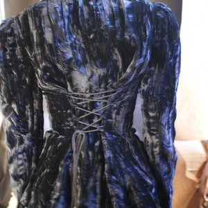 Può includere: Una giacca di velluto nero con un corpetto aderente e una schiena con lacci. La giacca ha una gonna leggermente svasata ed è realizzata in un tessuto morbido e lussuoso.