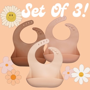 May include: Set of three silicone baby bibs with a pocket to catch food. The bibs are in shades of brown and beige.