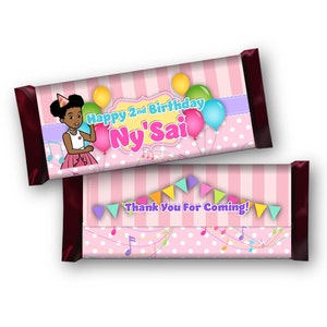May include: Pink and white striped chocolate bar wrapper with a cartoon girl wearing a party hat and holding balloons. The text on the wrapper says "Happy 2nd Birthday Ny'Sai". The back of the wrapper has a pink and white striped background with musical notes and the text "Thank You For Coming!"