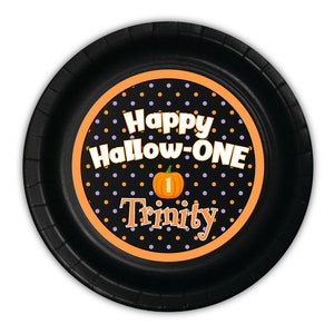 May include: Black paper plate with an orange and purple polka dot circle design. The circle says "Happy Hallow-ONE" with a small pumpkin and the number "1" inside. The name "Trinity" is written below the pumpkin.