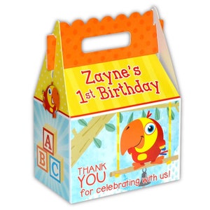 May include: A colorful party favor box with a parrot design. The box is orange, yellow, blue, and green. It says "Zayne's 1st Birthday" and "Thank You for celebrating with us!"