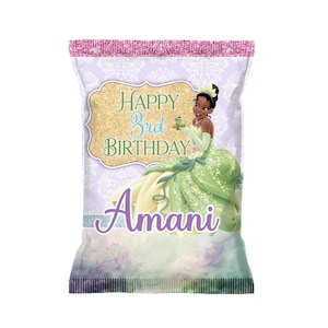 May include: A custom-designed party favor bag featuring a princess in a green gown. The bag has the text "Happy 3rd Birthday Amani" in a decorative font. The background is a light purple with a floral pattern, and the top is glittery pink.
