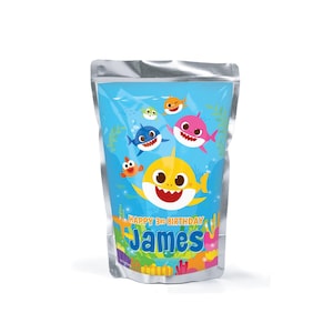 Könnte beinhalten: Ein blauer Beutel mit einem Cartoon-Hai-Familien-Design. Der Beutel trägt den Text "HAPPY 3RD BIRTHDAY James" in Blau und Weiß. Das Design umfasst gelbe, rosa, blaue und orange Haie mit Unterwasserpflanzen.