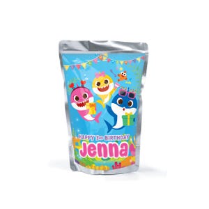 Könnte beinhalten: Ein silberner Beutel mit einem farbenfrohen Design von Cartoon-Haien. Der Beutel trägt den Text "Happy 3rd Birthday Jenna" in Pink und Gelb. Der Hintergrund ist blau mit Unterwasserelementen.