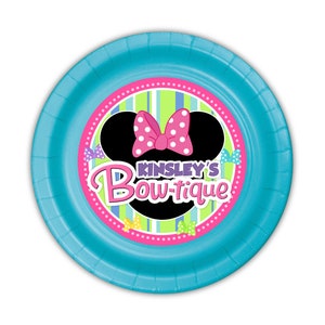 Puede incluir: Un plato de papel redondo azul claro con un dise&ntilde;o de Minnie Mouse. El centro presenta una silueta negra de la cabeza de Minnie con un lazo rosa de lunares. El texto "Kinsley's Bow-tique" se muestra en rosa y morado.