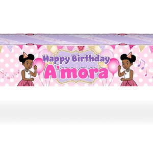 May include: A rectangular pink tablecloth with a polka dot pattern and the words "Happy Birthday A'mora". The tablecloth features illustrations of a girl, balloons, and musical notes. The table has black metal legs.
