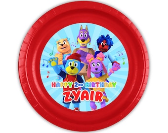 May include: A round red paper plate featuring a central graphic of five colorful cartoon animal characters against a light blue sunburst background. The text reads HAPPY 2ND BIRTHDAY ZYAIR in multi-colored letters with musical notes.