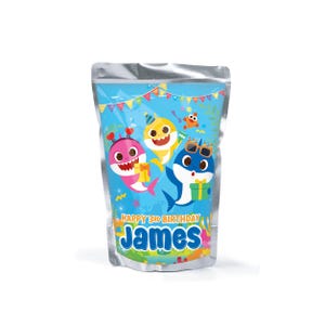May include: A silver pouch featuring a colorful design with three cartoon sharks. The sharks are in party hats and sunglasses, with the text "HAPPY 3RD BIRTHDAY JAMES" below. The background is blue with festive decorations.