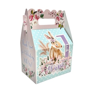 May include: A light blue and pink favor box with a white polka dot pattern. The box features a bunny rabbit illustration with a floral crown and the text "Sweet Bunny is one" and "Thank you for celebrating with us!" The box has a handle and a personalized name tag that says "Laiah".