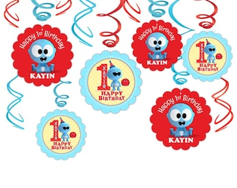 May include: A set of 6 blue and red swirl hanging decorations for a first birthday party. The decorations feature a cartoon baby character with the text "Happy 1st Birthday" and the name "Kayin".