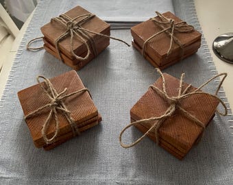 Può includere: Quattro set di sottobicchieri quadrati in legno legati insieme con lo spago. I sottobicchieri sono di colore marrone chiaro e sono disposti su un sottopentola grigio con cuciture bianche.