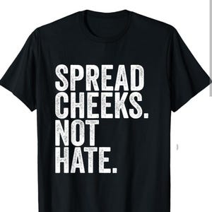 以下が含まれることがあります： 白い文字で「SPREAD CHEEKS. NOT HATE.」と書かれた黒いTシャツ
