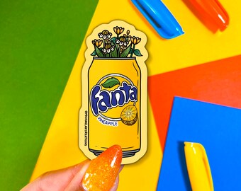 Könnte beinhalten: Ein gelber und weißer Aufkleber mit einer Dose Fanta Ananas-Soda, aus der ein Blumenstrauß wächst. Der Aufkleber trägt den Text "Fanta Ananas" und "GPICHAELKCREATIONS".