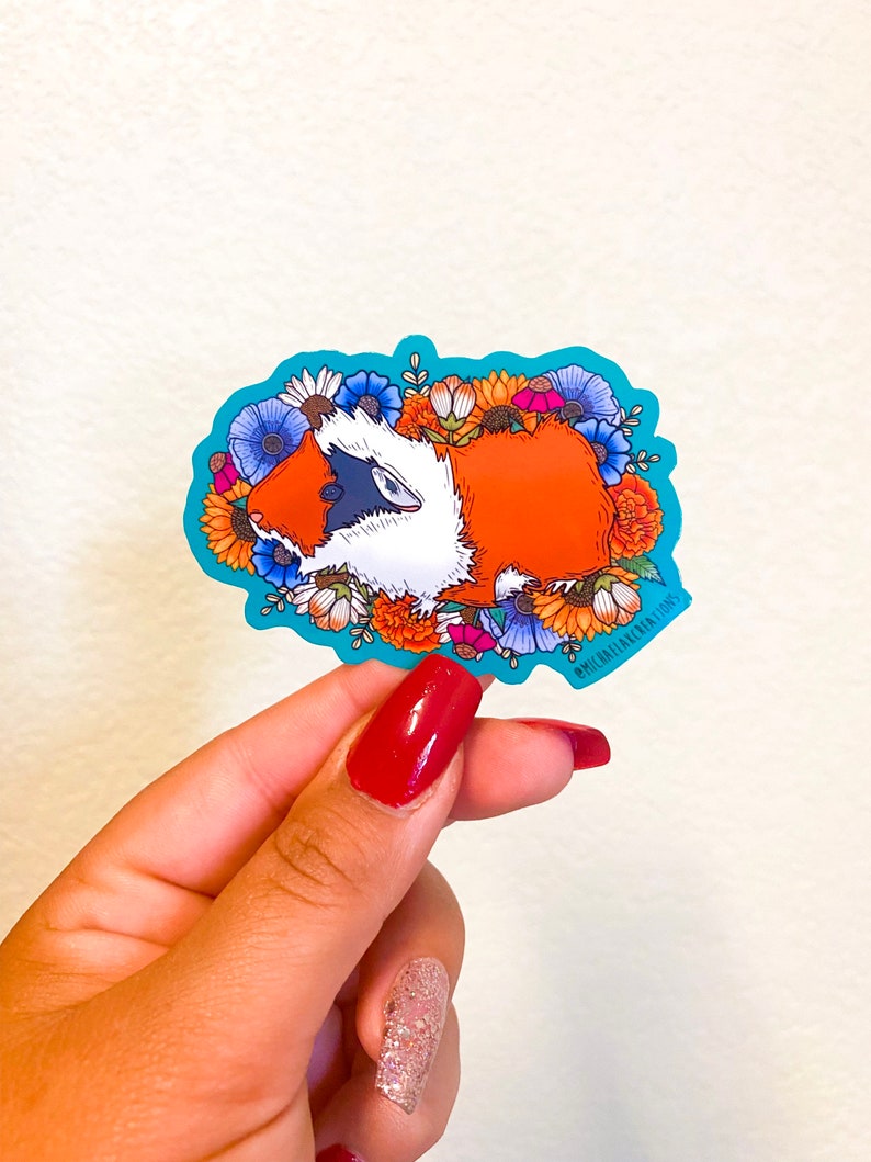 Puede incluir: Una pegatina con un conejillo de indias de dibujos animados rodeado de flores coloridas. El conejillo de indias es naranja y blanco con ojos negros y una nariz rosa. Las flores son de varios colores, incluyendo rojo, amarillo, naranja, azul y morado. La pegatina est&aacute; sobre un fondo turquesa.