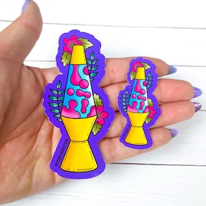 May include: Two purple stickers with a retro-style lava lamp design. The larger sticker has a yellow base, blue and pink lava, and pink flowers. The smaller sticker is the same design but smaller. Both stickers have the text "@STICKYWELLCOLLECTIBLES" on the bottom.