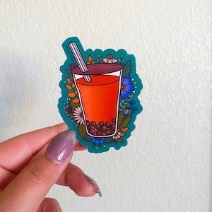 K&ouml;nnte beinhalten: Ein Aufkleber mit einem Glas Bubble Tea mit einem Strohhalm, umgeben von bunten Blumen auf einem t&uuml;rkisfarbenen Hintergrund.