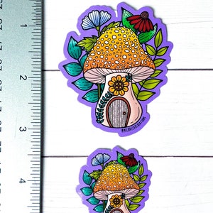 May include: Two purple and white mushroom house stickers with yellow and orange spots. The mushroom houses have a small door and a sunflower on the front. The stickers are surrounded by green leaves and flowers.