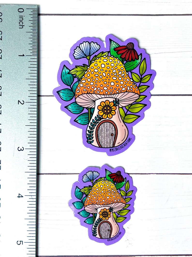 May include: Two purple and white mushroom house stickers with yellow and orange spots. The mushroom houses have a small door and a sunflower on the front. The stickers are surrounded by green leaves and flowers.